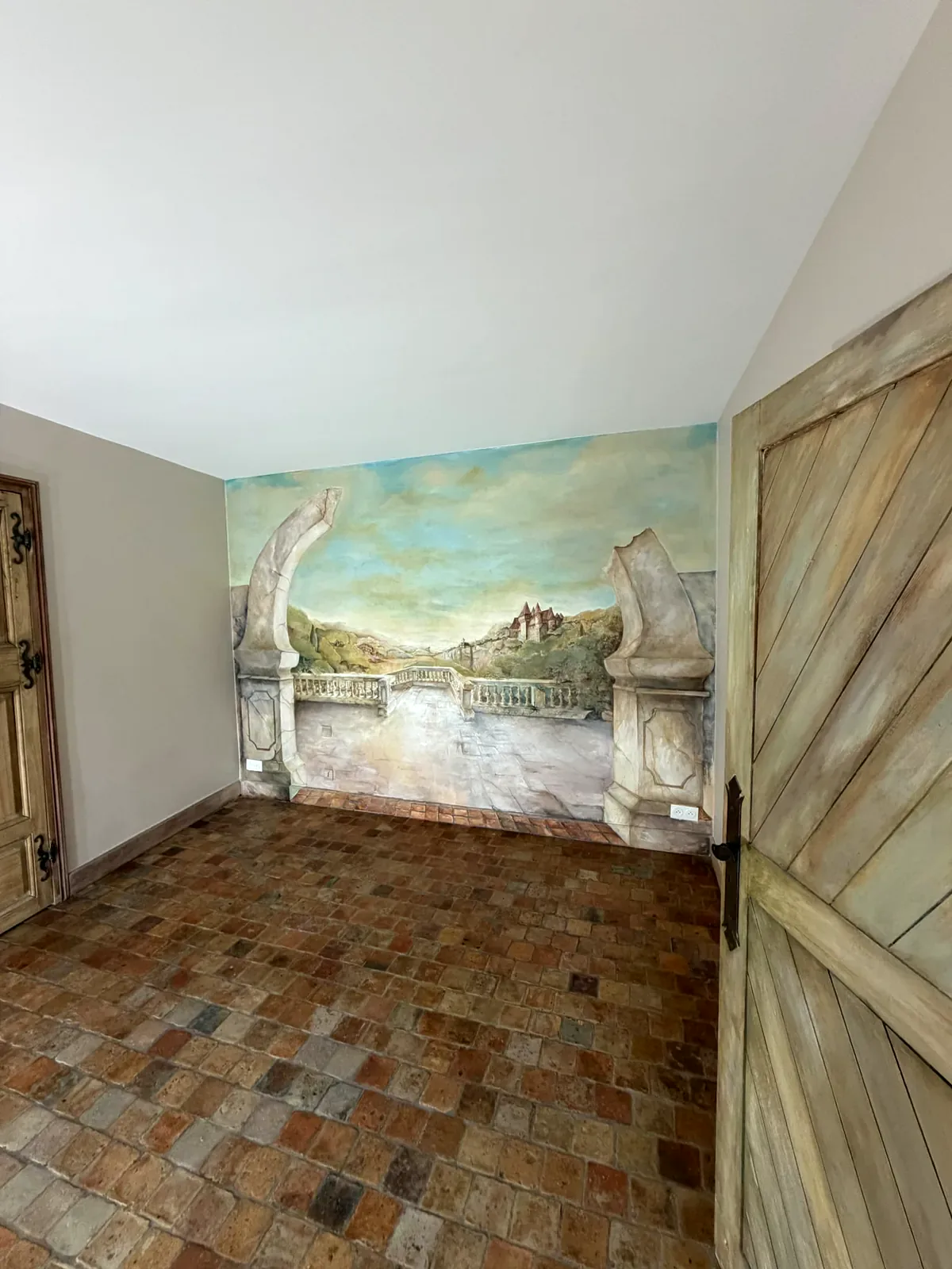 Pièce rénovée avec décor mural panoramique, sol en tomettes et portes en bois